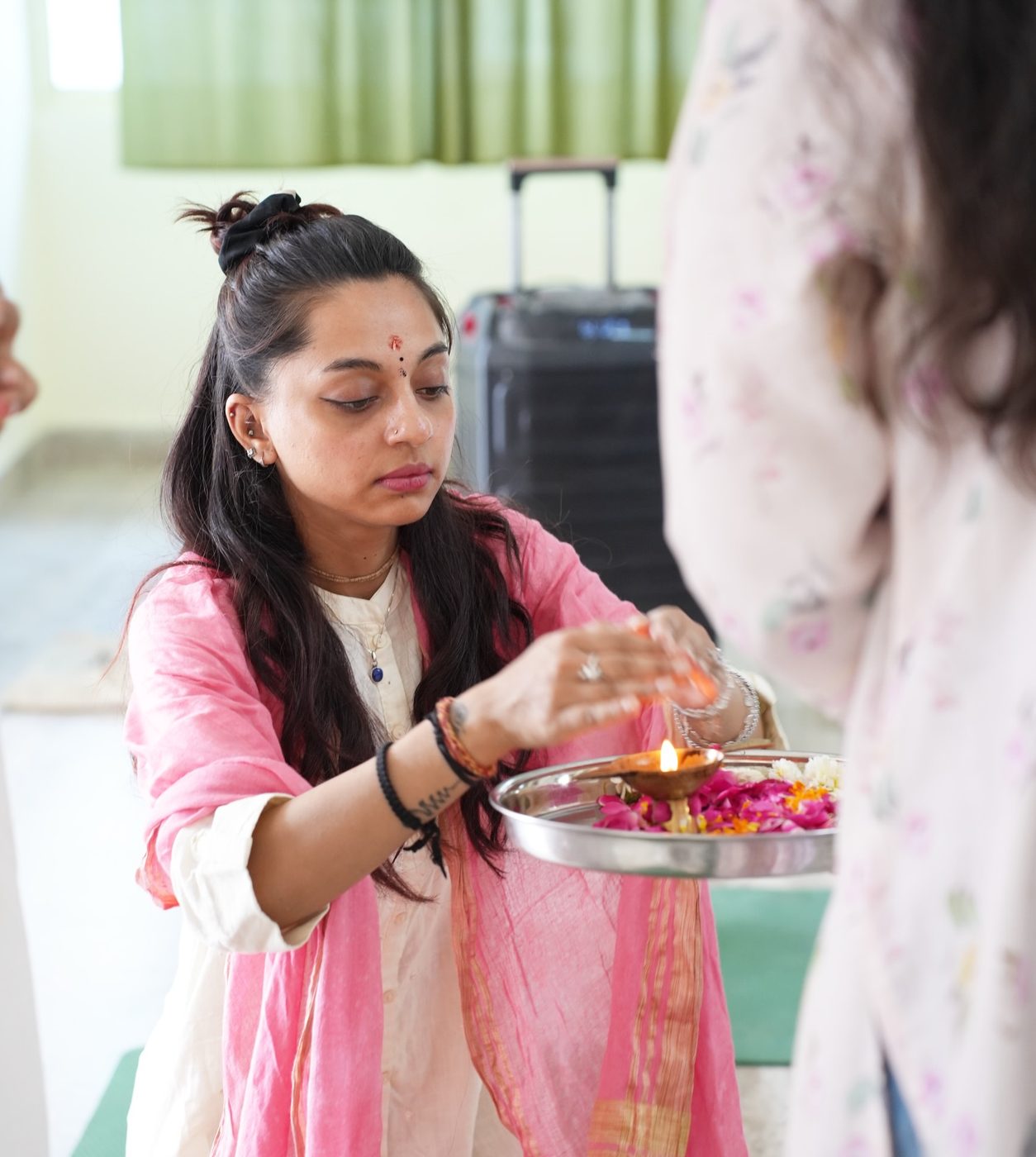 Harshita performing aarti with a lit diya on a flower-filled tray
