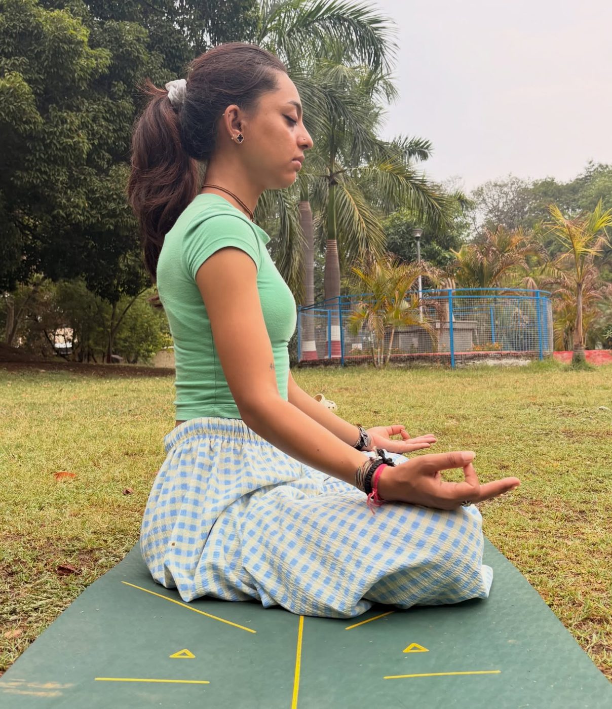 Harshita meditating cross-legged on a mat in a park