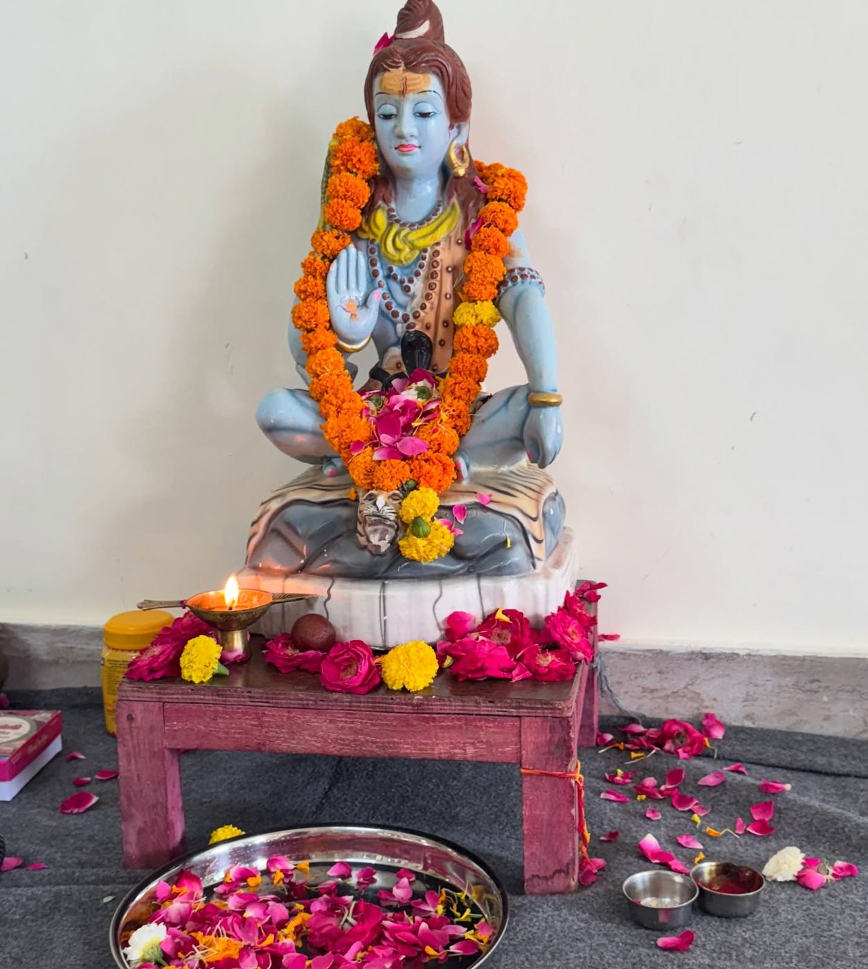 A garlanded Shiva statue with a lit diya and offering plates